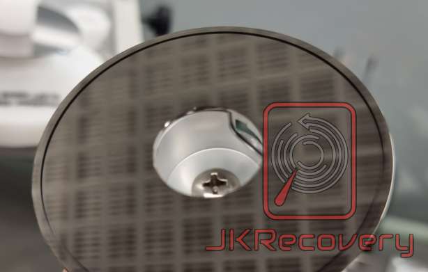 Zbliżenie na talerz dysku twardego HDD z widocznym centrum mocowania i śrubą, logo JKRecovery w prawym dolnym rogu