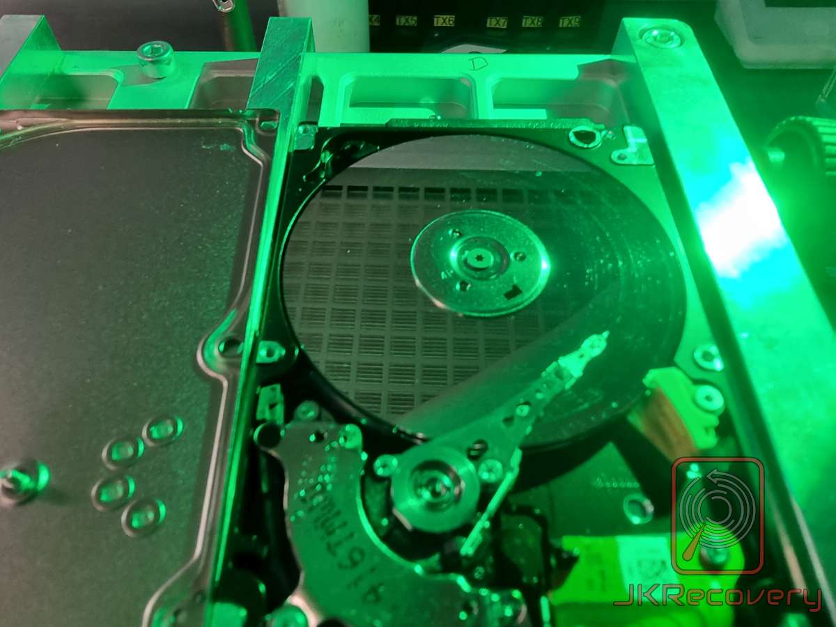 Otwarty dysk twardy HDD oświetlony zielonym światłem UV w laboratorium odzysku danych JKRecovery – widoczny talerz magnetyczny oraz ramię głowicy odczytu/zapisu