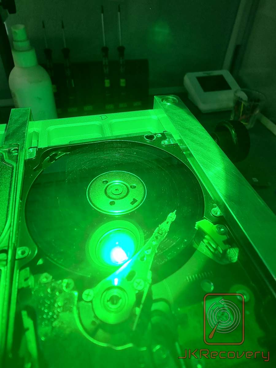 Otwarty dysk twardy HDD oświetlony zielonym światłem UV w komorze czystej, widoczny talerz magnetyczny i głowica odczytu/zapisu podczas procesu odzysku danych