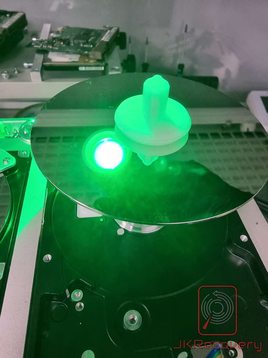 Talerz magnetyczny dysku twardego HDD wyjęty z obudowy, umieszczony na specjalnym adapterze z uchwytem do przenoszenia, oświetlony zielonym światłem UV podczas procesu odzysku danych