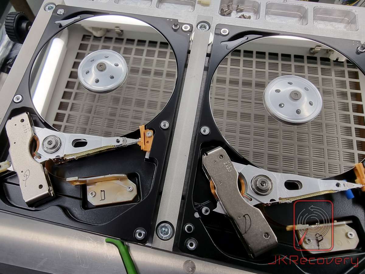Dwa otwarte dyski twarde HDD w komorze czystej, widoczne talerze magnetyczne i ramiona głowic odczytująco-zapisujących, prawdopodobnie podczas procedury odzysku danych przez laboratorium JKRecovery
