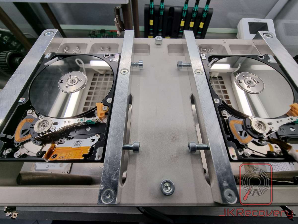 Dwa otwarte dyski twarde HDD umieszczone w specjalistycznym metalowym statywie laboratoryjnym, jeden z dysków ma uniesione ramię aktuatora z głowicami poza powierzchnią talerza
