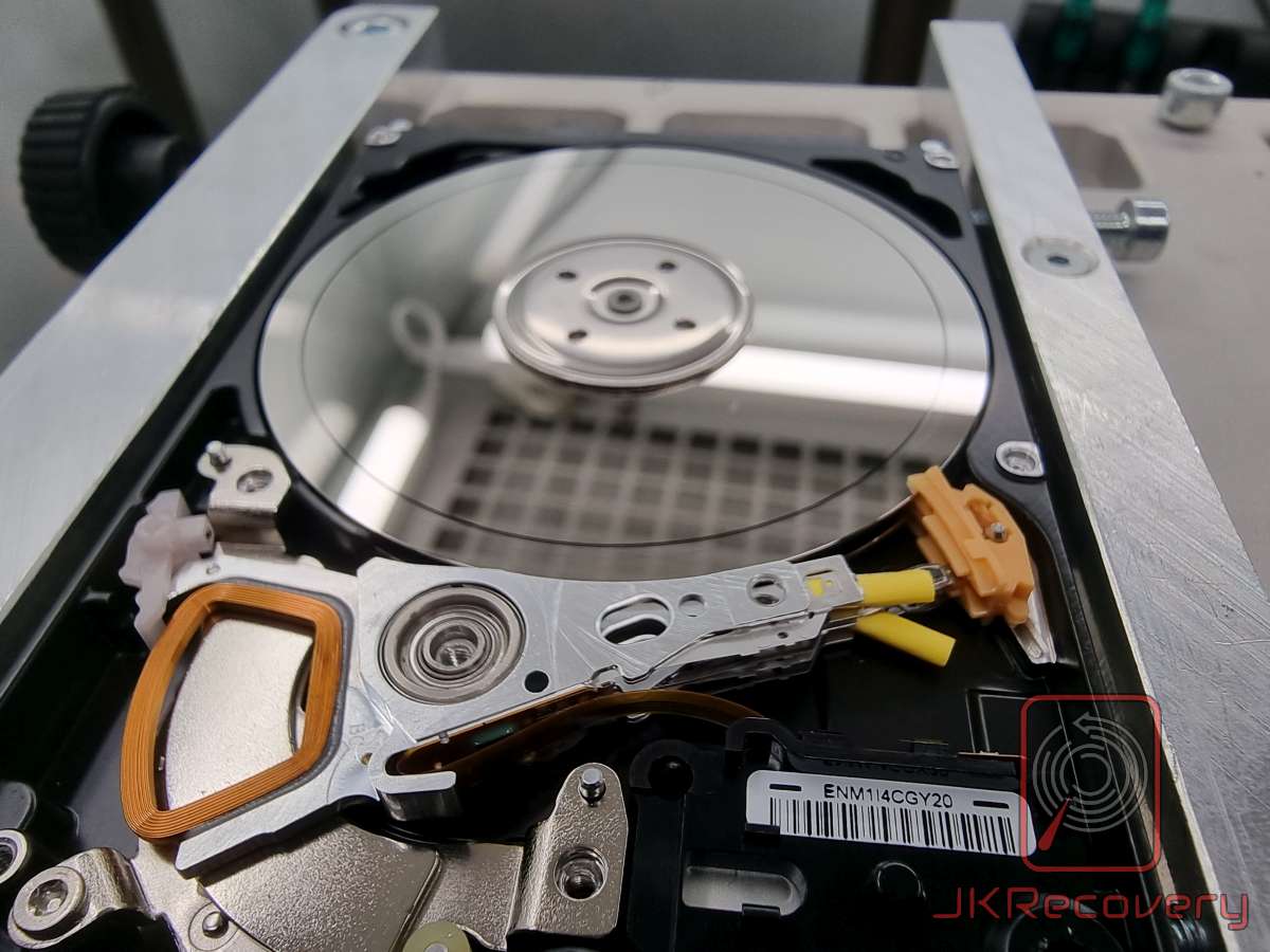 Otwarty dysk HDD w uchwycie laboratoryjnym podczas diagnostyki — widok platterów i ramienia głowic