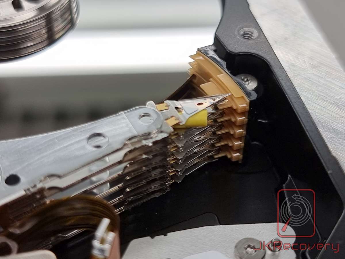 Zbliżenie na zniszczony pakiet głowic dysku twardego z poważnymi uszkodzeniami mechanicznymi i zanieczyszczeniami, widoczne odkształcone i sklejone listwy zawieszenia głowic