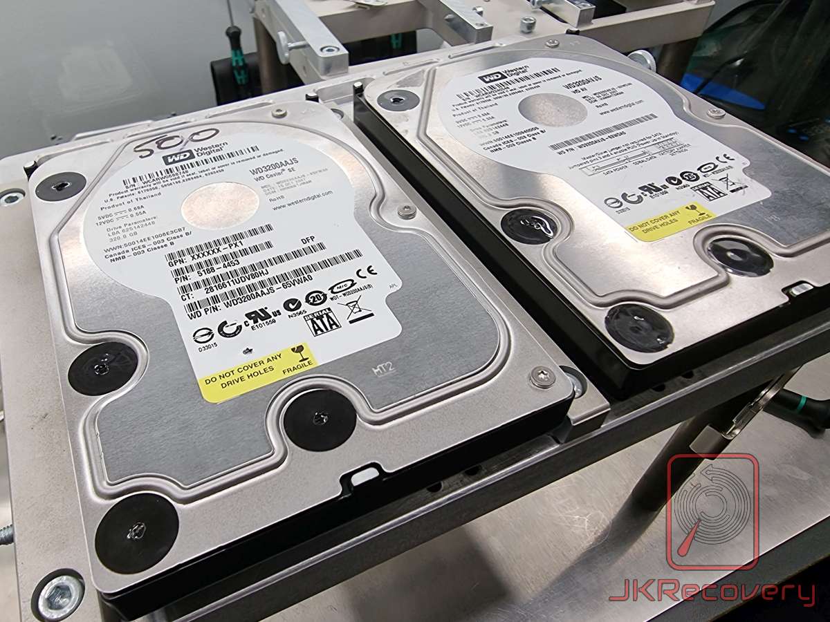 Dwa dyski twarde Western Digital WD3200AAJS Caviar SE 320GB w formacie 3.5 cala umieszczone na metalowym stojaku w laboratorium odzysku danych JKRecovery. Na dyskach widoczne etykiety z ostrzeżeniem DO NOT COVER ANY DRIVE HOLES oraz oznaczenia FRAGILE.