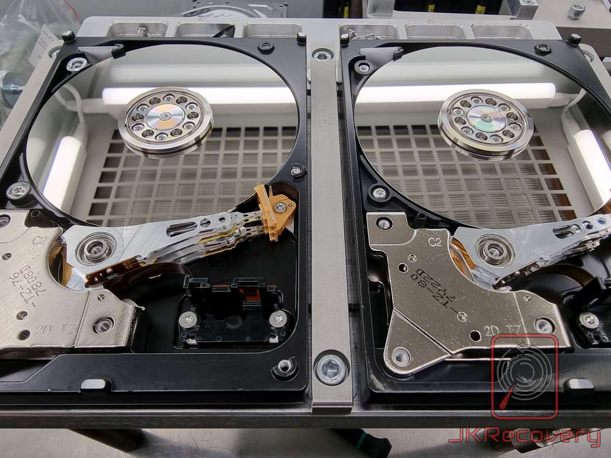 Dwa otwarte dyski twarde Western Digital umieszczone w specjalnym uchwycie laboratoryjnym. Lewy dysk ma uszkodzone głowice z widocznym pomarańczowym uchwytem, prawy dysk posiada zdemontowany zespół głowic. Procedura wymiany głowic w komorze czystej.