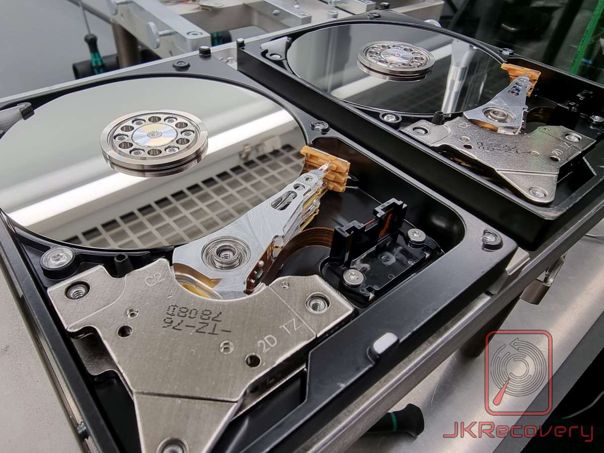 Dwa otwarte dyski twarde HDD w laboratorium odzysku danych - widok z góry na talerze magnetyczne, zespół głowic z wieloma ramionami oraz mechanizm aktuatora z cewką głosową