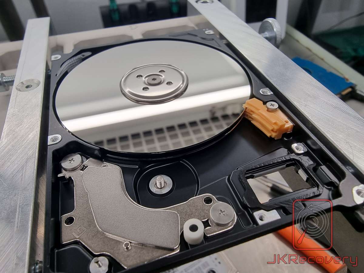 Otwarty dysk twardy HDD w uchwycie laboratoryjnym, widok z góry na talerz magnetyczny oraz mechanizm siłownika głowic bez taśmy FPC – dysk po częściowym demontażu