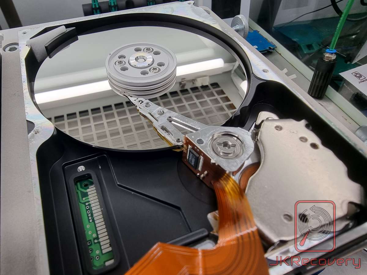 Wnętrze otwartego dysku twardego HDD z widocznym talerzem magnetycznym, ramieniem odczytu/zapisu z głowicą oraz złączem interfejsu. Dysk umieszczony w komorze czystego powietrza podczas procedury odzysku danych przez JKRecovery.