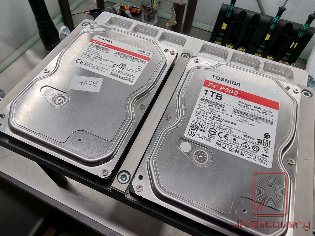 Dwa dyski twarde Toshiba PC P300 1TB 7200rpm z buforem 64MB model HDWD110 leżące obok siebie na metalowej powierzchni roboczej w laboratorium odzysku danych JKRecovery, jeden z nalepką z numerem 7006
