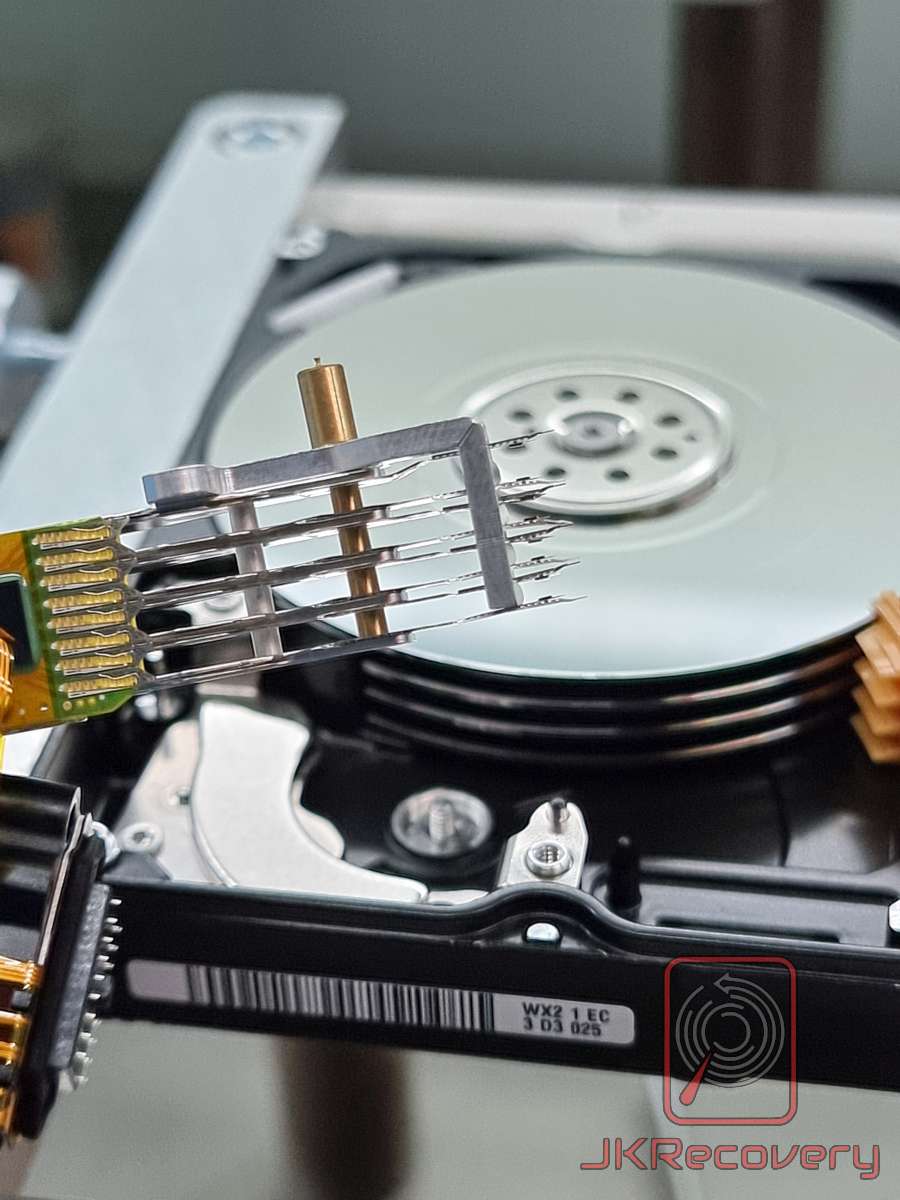 Zbliżenie na zespół głowic odczytująco-zapisujących dysku twardego HDD z widocznym ramieniem aktuatora, talerzami i elastyczną taśmą FPC w laboratorium odzysku danych JKRecovery