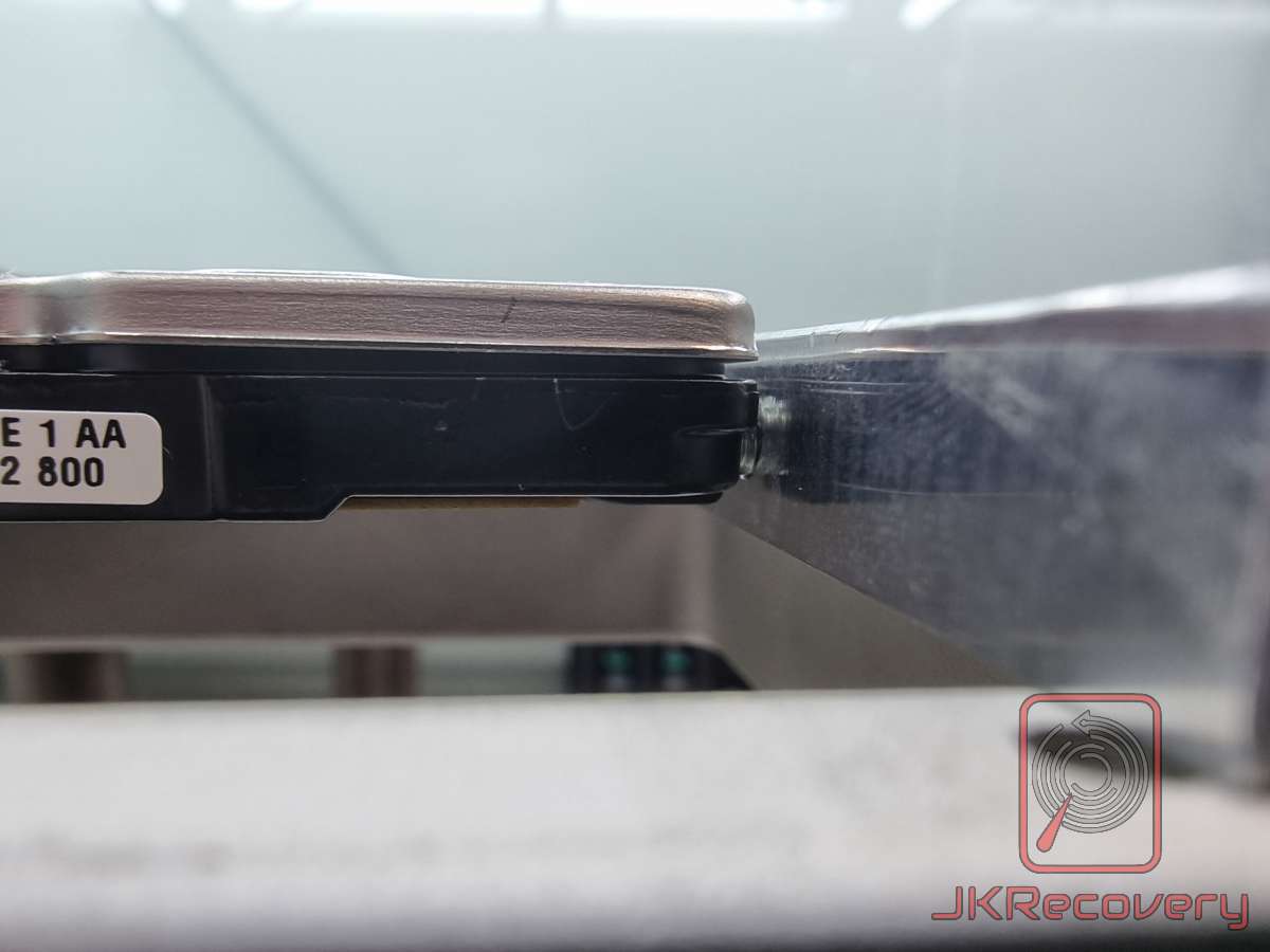 Widok boczny uszkodzonego dysku twardego HDD z wyraźnie widocznym rozerwaniem i deformacją obudowy w miejscu łączenia górnej pokrywy z korpusem. Obudowa jest pęknięta i odgięta, co wskazuje na poważne uszkodzenie mechaniczne dysku.