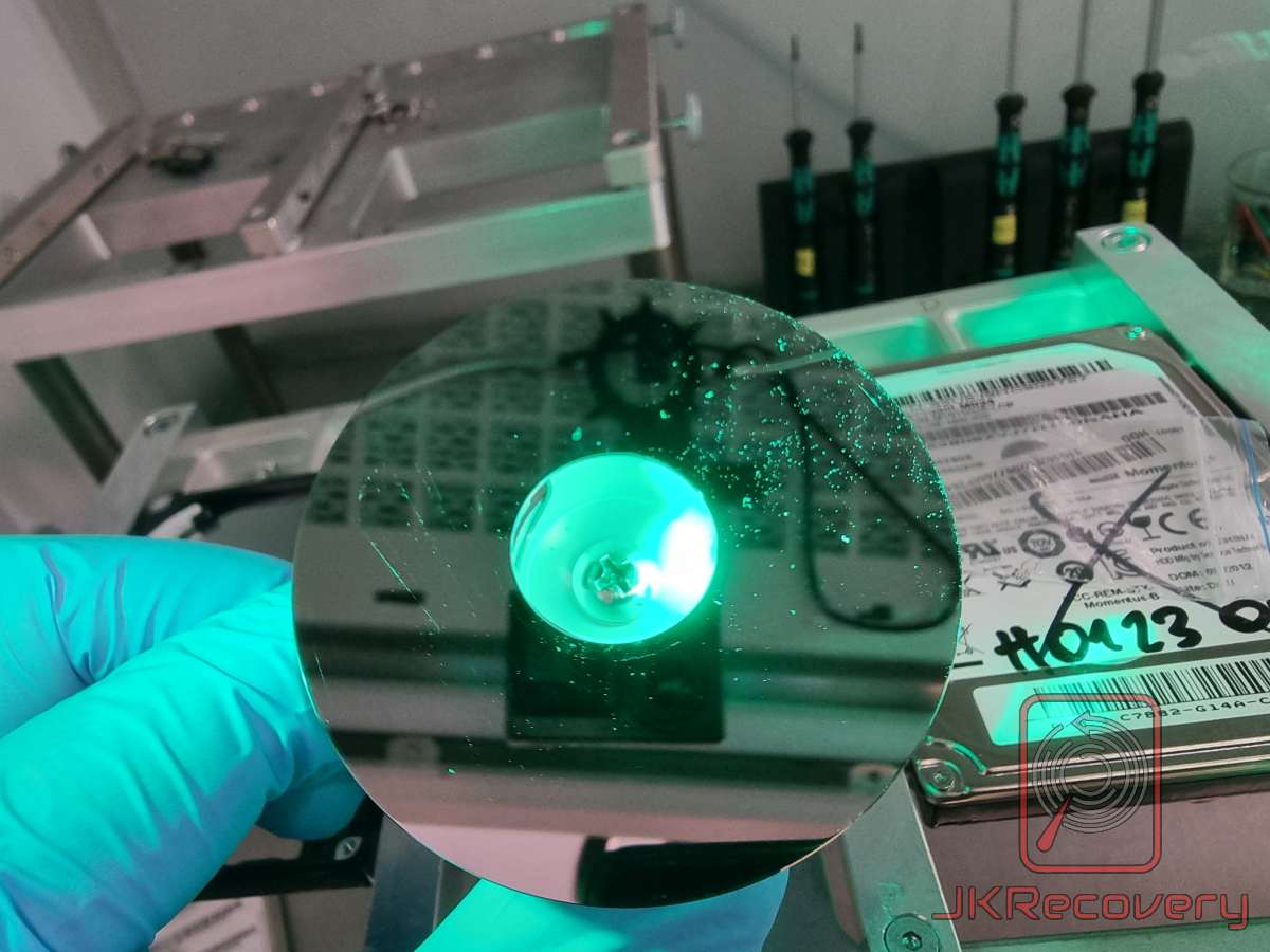 Plater magnetyczny dysku HDD w świetle UV — widoczne ślady zarysowań po head crash, powierzchnia oceniana po otwarciu w komorze ISO 5