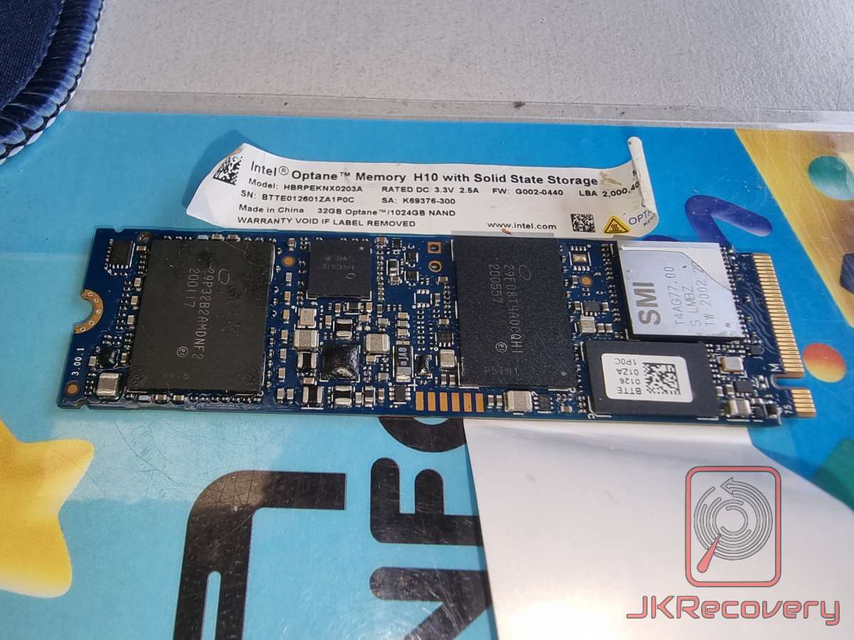 Intel Optane Memory H10 z pamięcią SSD - model HBRPEKNX0203A, 32GB Optane + 1024GB NAND, widok PCB od góry z etykietą producenta, kontroler SMI oraz układy pamięci NAND widoczne na płytce