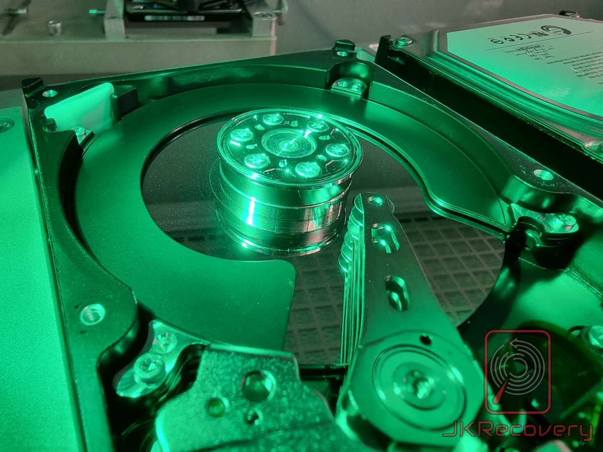 Wnętrze otwartego dysku twardego HDD oświetlone zielonym światłem, widoczny talerz dysku oraz piasta silnika wrzecionowego z bliska