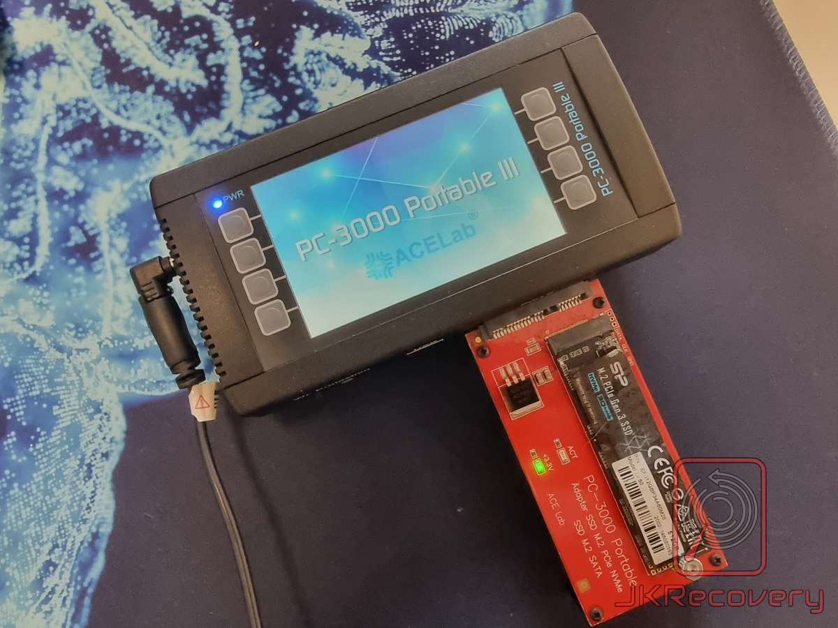 Urządzenie ACELab PC-3000 Portable III z podłączonym dyskiem SSD M.2 NVMe firmy Silicon Power na czerwonej karcie adaptera PC-3000 Portable Adapter SSD M.2 PCIe NVMe/SATA, leżące na niebieskiej podkładce na biurko