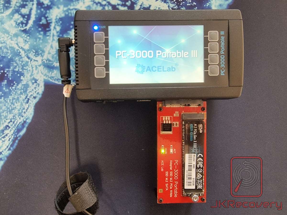 Urządzenie ACELab PC-3000 Portable III podłączone do czerwonej karty adaptera SSD M.2 PCIe NVMe z zamontowanym dyskiem Silicon Power M.2 PCIe Gen 3 SSD 512GB, leżące na niebieskiej podkładce