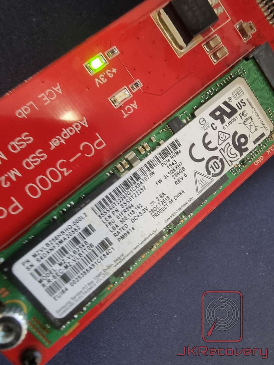 Zbliżenie na dysk SSD M.2 NVMe Samsung PM981a 256GB (PCIe NVMe, model MZ-VLB256B) zamontowany w czerwonym adapterze PC-3000 SSD M.2 firmy ACE Lab z widoczną zieloną diodą zasilania +3.3V