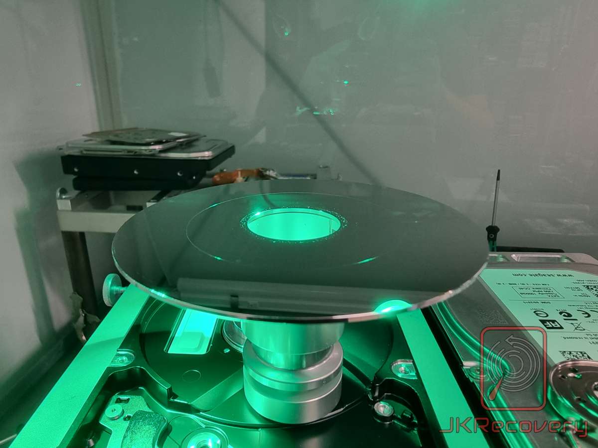 Talerz dysku twardego HDD zamontowany na uchwycie w komorze czystego pomieszczenia, oświetlony zielonym światłem UV podczas procesu odzysku danych