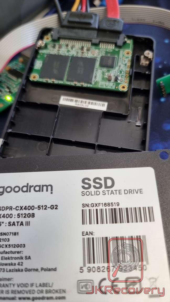 Otwarty dysk SSD Goodram CX400 512GB SATA III z widoczną płytką PCB i układami pamięci flash, podłączony do zestawu diagnostycznego w laboratorium odzysku danych JKRecovery
