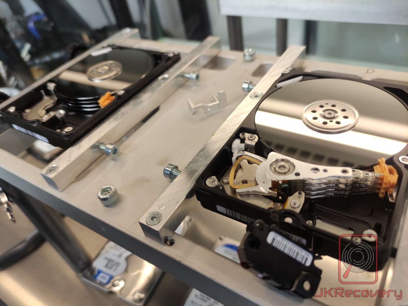 Dwa otwarte dyski twarde HDD zamontowane w metalowym stanowisku laboratoryjnym, widoczne talerze magnetyczne, ramiona głowic oraz wiązki kabli flex podczas procesu odzysku danych