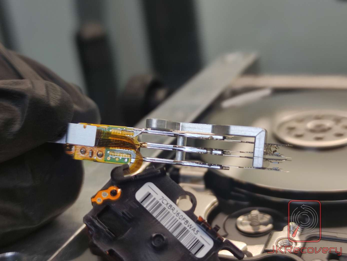 Zbliżenie na uszkodzone głowice odczytująco-zapisujące wyjęte z otwartego dysku twardego, trzymane w rękawiczce przez technika laboratorium odzysku danych JKRecovery
